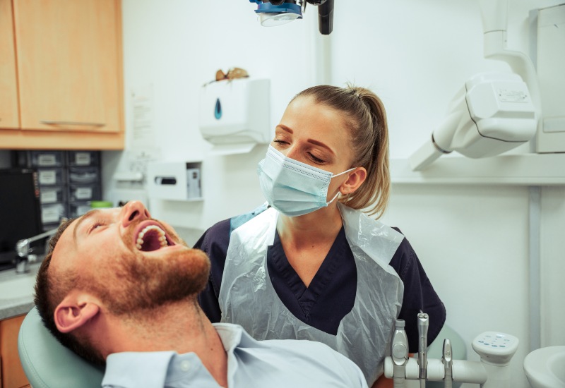 A dentist wearing a mask examines a male patient’s teeth in a dental clinic in Southfield, MI